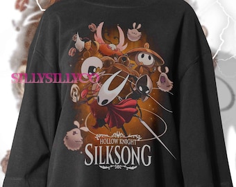 May include: Black t-shirt featuring a colorful graphic from the video game Hollow Knight: Silksong. The design includes various characters and the game's logo in white. The shirt has a relaxed fit.