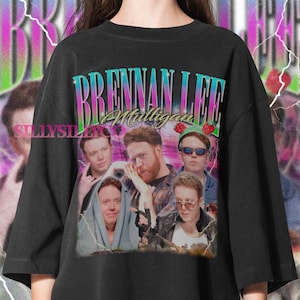 May include: Black crew neck t-shirt featuring a graphic design with the text "Brennan Lee Mulligan" in a colorful, retro font. The design includes multiple images of a person. The shirt has a vintage, distressed look.