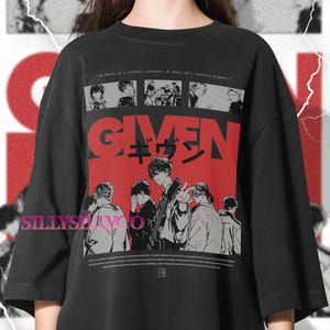 Può includere: T-shirt nera con grafica rossa con la scritta "GIVEN" e caratteri giapponesi. Il design include illustrazioni in stile manga. Il testo in alto recita "A story of a certain summer. A story of a certain night."