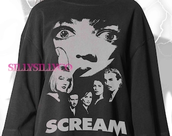 May include: Black t-shirt featuring a grayscale graphic of the movie "Scream". The design includes a close-up of a face with wide eyes, and the word "SCREAM" in large, bold letters. The shirt also features images of the movie's cast.