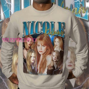 Puede incluir: Sudadera beige con un collage de im&aacute;genes de Nicole Kidman y el nombre "Nicole Kidman" en texto azul y amarillo. El dise&ntilde;o incluye gr&aacute;ficos de rayos y una est&eacute;tica vintage.