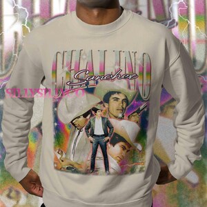 Puede incluir: Sudadera beige con un gr&aacute;fico de Chalino S&aacute;nchez con sombrero de vaquero y el nombre "Chalino S&aacute;nchez" en una fuente estilizada. El dise&ntilde;o incluye m&uacute;ltiples im&aacute;genes del cantante con un fondo colorido.