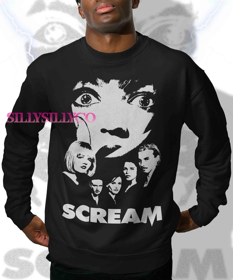 May include: Black sweatshirt with a white graphic from the film "Scream." The design features a large face with wide eyes, a knife, and the word "SCREAM." Below the face are images of the movie's cast. A classic horror movie design.