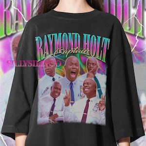 May include: Black t-shirt featuring a colorful graphic of Raymond Holt, with the text "Raymond Holt Captain" in a retro style. The design includes multiple images of the character in various poses. The shirt has a vintage, distressed look.