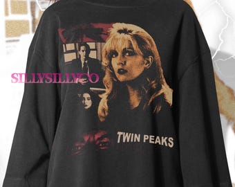 Może przedstawiać: Czarny t-shirt z grafiką w stylu retro z serialu Twin Peaks. Projekt zawiera obrazy postaci i tytuł serialu w białych literach. Koszulka ma krótkie rękawy i luźny krój.