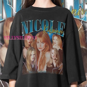 Puede incluir: Camiseta negra de gran tama&ntilde;o con un dise&ntilde;o gr&aacute;fico de Nicole Kidman. El dise&ntilde;o presenta el texto "NICOLE Kidman" en azul y amarillo, junto con m&uacute;ltiples im&aacute;genes de la actriz. El dise&ntilde;o tiene una est&eacute;tica vintage con acentos de rayos.