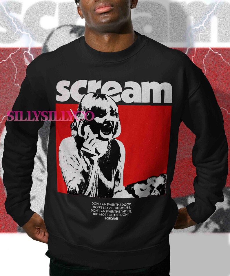 May include: Black sweatshirt with the word "scream" in white block letters above a red rectangle. Inside the rectangle is a black and white image of a person. Below the image is text that reads "DON'T ANSWER THE DOOR...SCREAM!"