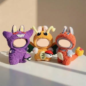 Könnte beinhalten: Drei Plüsch-Charakterkostüme in Lila, Orange und Rot. Die Kostüme haben hasenartige Ohren und offene Gesichtsflächen. Das orangefarbene Kostüm hält einen kleinen Ball. Die Kostüme befinden sich auf einer weißen Oberfläche.