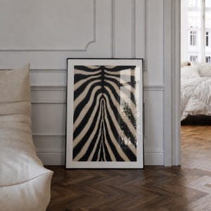 May include: A rectangular framed wall art piece featuring a high-contrast black and beige zebra stripe pattern. The print is encased in a thin black frame, displaying a symmetrical arrangement of vertical, curved animal print lines across the surface.