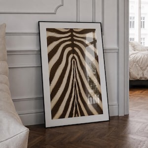 May include: A rectangular framed wall art piece featuring a high-contrast zebra stripe pattern in dark brown and cream. The print is encased in a thin black frame with a white mat border, displaying a symmetrical, organic animal fur texture.