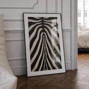 May include: A rectangular framed wall art piece featuring a high-contrast black and off-white zebra stripe pattern. The print is encased in a thin black frame, displaying a symmetrical arrangement of vertical, wavy animal fur stripes.