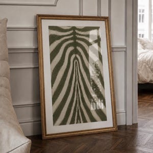 May include: A rectangular framed wall art piece featuring a vertical abstract pattern of alternating olive green and off-white stripes that mimic a zebra print. The artwork is enclosed in a thin, metallic gold frame with a wide white mat border.