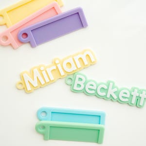 Op de afbeelding: Vier kleurrijke plastic naamstickers met witte letters. De namen zijn Miriam, Beckett en twee blanco stickers.
