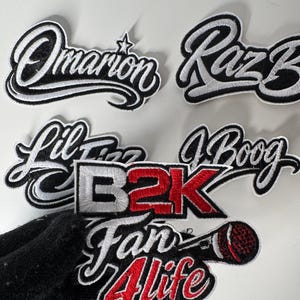 May include: Embroidered patches with various names and phrases in a script font. The patches feature black and white or red and white color schemes. The patches include the names "Omarion", "Raz B", "Lil Fizz", and "J Boog", as well as the phrases "B2K" and "Fan 4 Life".
