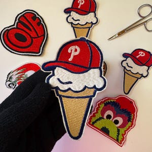 May include: Embroidered patches including a red baseball cap with a white "P" on an ice cream cone, a red heart with "LOVE" text, and a green monster face. A pair of small scissors is also visible.