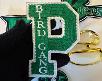May include: Green and white embroidered patches with the text "BIRD GANG" and "215 PHILLY". The patches include a large green letter "P" and a green letter "B". Also included are gold-rimmed eyeglasses.
