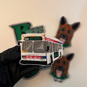 May include: Embroidered patches featuring a bus with "108 GO BIRDS" text, a green "BIRDS" patch, and two dog head patches. The bus patch has "NO ONE LIKES US" text. The patches are in various colors.