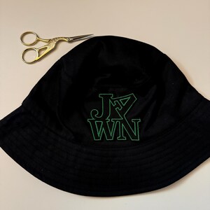 May include: Black bucket hat with a green embroidered logo that says "J.Y. WIN".