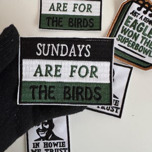 Könnte beinhalten: Gestickte Aufnäher mit Text. Zwei Aufnäher lesen "SUNDAYS ARE FOR THE BIRDS" in weißen Buchstaben auf einem schwarzen, weißen und grünen Hintergrund. Andere Aufnäher enthalten "JUST A REMINDER EAGLES WON THE SUPERBOWL" und "IN HOWIE WE TRUST".