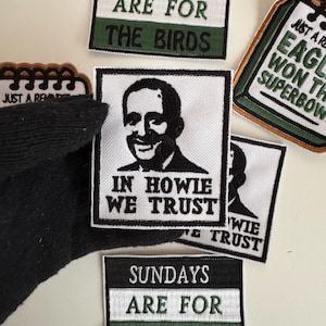 May include: Several embroidered patches with text and designs. One patch says "SUNDAYS ARE FOR THE BIRDS" in white text on a black and green background. Another patch features a portrait and the text "IN HOWIE WE TRUST".