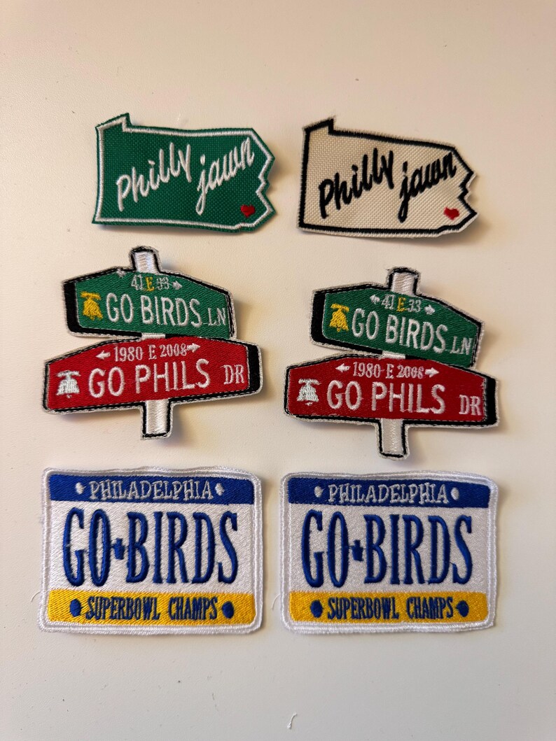 May include: A collection of embroidered patches featuring Philadelphia sports team themes. Includes patches with "Philly Jawn", "Go Birds", "Go Phils", and "Superbowl Champs" text. The patches are in green, red, blue, and white.