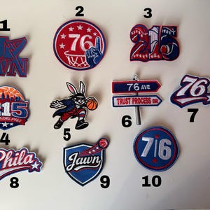 Könnte beinhalten: Eine Sammlung von zehn gestickten Aufnähern mit verschiedenen Designs. Die Aufnäher zeigen die Zahlen "76", "215" und das Wort "Phila", zusammen mit Basketball-Grafiken und einer Hasenfigur.