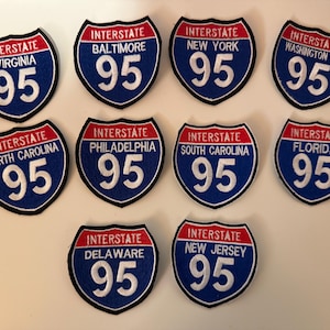Puede incluir: Diez parches bordados con forma de señales de autopista Interstate 95. Cada parche presenta una franja superior roja con la palabra INTERSTATE, un campo azul con un nombre de lugar específico y el número 95 en blanco, con borde negro.