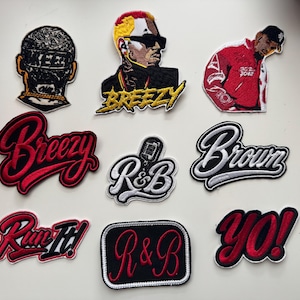 May include: A collection of nine embroidered patches featuring various designs including portraits of a person, the text BREEZY, Brown, R&B, Run It!, and YO!, along with a microphone icon. The patches utilize a color palette of red, black, white, and yellow.
