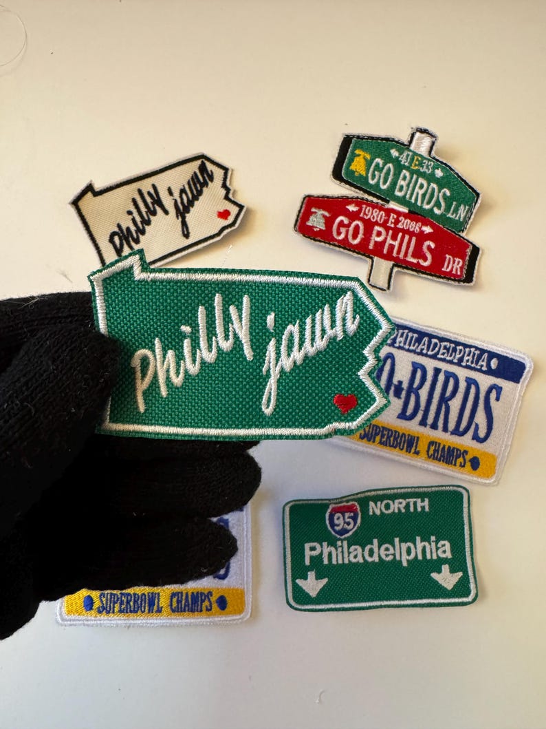 May include: A collection of embroidered patches with Philadelphia-themed designs. The patches feature phrases like "Philly Jawn," "Go Birds," and "Go Phils," along with a road sign for Philadelphia. Some patches include "Superbowl Champs."