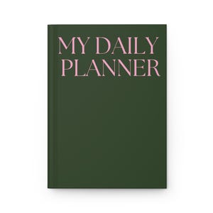 Könnte beinhalten: Ein dunkelgrüner Planer mit dem Text "MY DAILY PLANNER" in rosa Schrift.