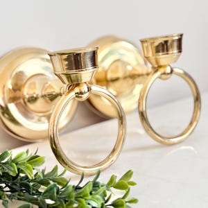 May include: A pair of gold metal wall mounted candle holders with ring handles.