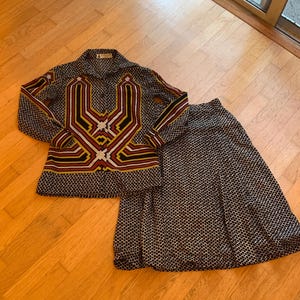 Puede incluir: Un conjunto vintage de dos piezas con una camisa de manga larga y una falda a juego. La camisa tiene un diseño geométrico en rojo, amarillo, negro y blanco. La falda y la camisa tienen un patrón repetitivo de pequeños diamantes blancos sobre fondo negro.