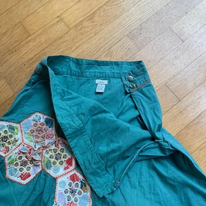 Pu&ograve; includere: Gonna color verde acqua con un design unico. La gonna presenta una serie di toppe esagonali colorate a motivi floreali. La vita ha due bottoni e cuciture arancioni. La gonna &egrave; realizzata in un tessuto morbido e fluido.