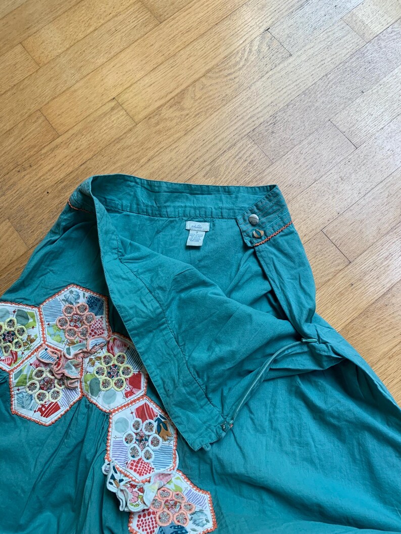 Pu&ograve; includere: Gonna color verde acqua con un design unico. La gonna presenta una serie di toppe esagonali colorate a motivi floreali. La vita ha due bottoni e cuciture arancioni. La gonna &egrave; realizzata in un tessuto morbido e fluido.