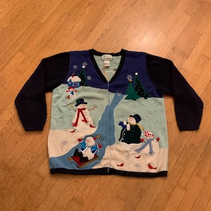 May include: A navy blue long-sleeve cardigan featuring a winter scene with appliqued snowmen, evergreen trees, a small house, and red birds. The front panels display a light blue and white snowy landscape with embroidered snowflakes and details.