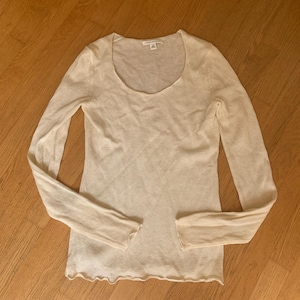 May include: A cream-colored long-sleeve shirt with a scoop neck. The shirt has a ribbed texture and a slightly ruffled hemline. The tag reads "Banana Republic".