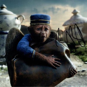 May include: A blue-clad monkey with a blue cap holds a brown leather suitcase. The monkey is wearing a blue uniform with a white collar and a blue cap. The suitcase is large and has a brown leather strap.