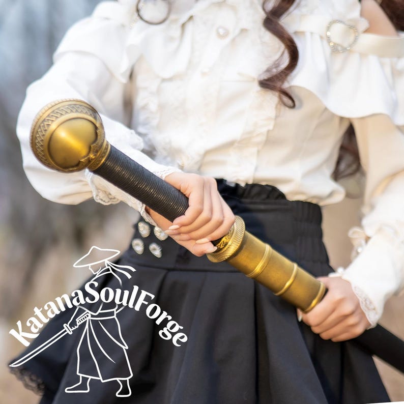 May include: A decorative sword with a gold-colored hilt and accents, a black handle, and a black blade. The sword is held in front of a person wearing a white blouse and black skirt. The Katana SoulForge logo is in the lower left corner.