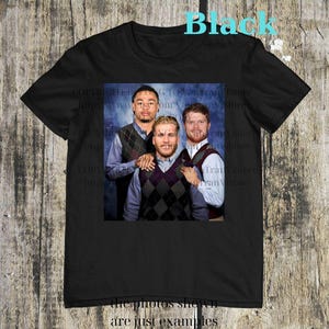 May include: Black t-shirt featuring a group photo of three people wearing argyle vests over button-down shirts. The word "Black" is printed in turquoise at the top, and the phrase "the photos shown are just examples" is at the bottom.