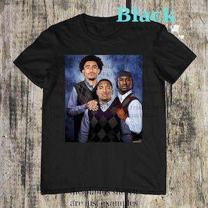 May include: Black t-shirt featuring a group photo of three people wearing argyle vests over collared shirts. The image has a blue background. The word "Black" is printed in turquoise at the top.