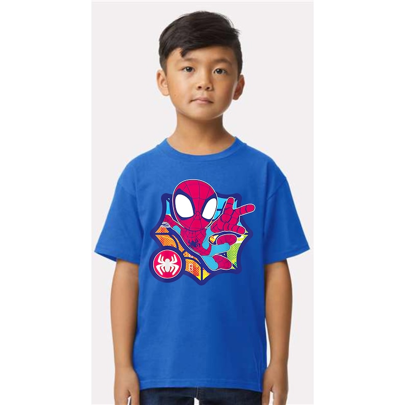 K&ouml;nnte beinhalten: Ein blaues T-Shirt mit einem Spider-Man-Motiv. Das Design zeigt eine rot-blaue Spider-Man-Figur in einer Web-Schleuder-Pose, vor einem Comic-Hintergrund. Ein Spider-Man-Logo ist ebenfalls sichtbar.