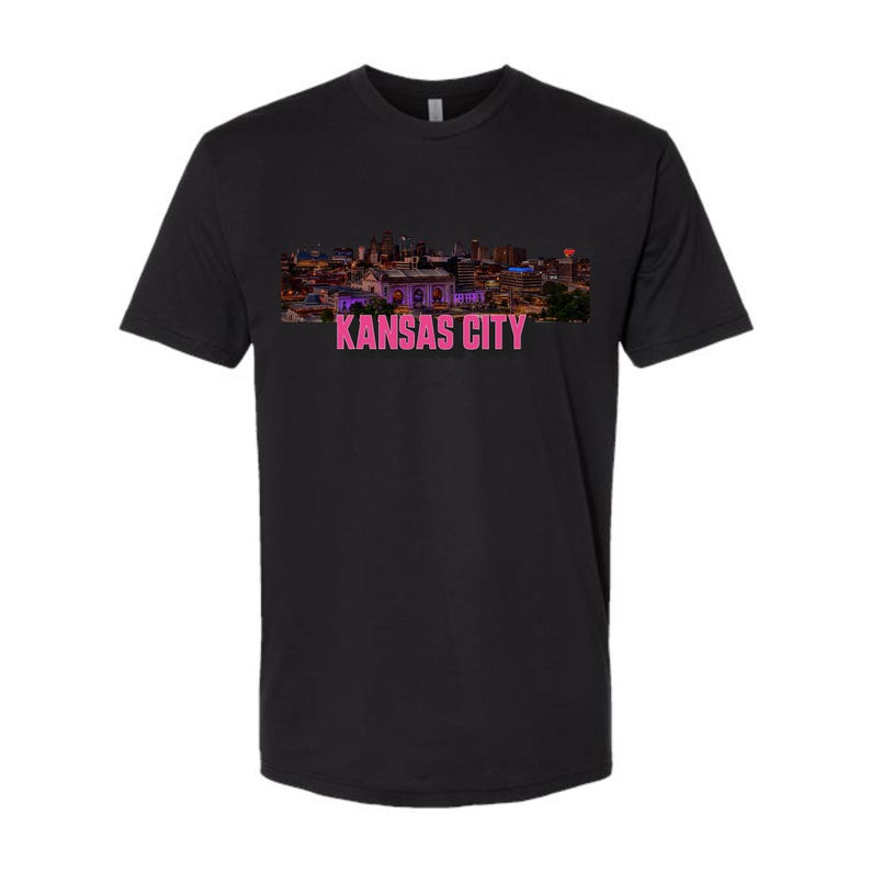 May include: Black t-shirt with a skyline image of Kansas City in pink and purple hues. The text "KANSAS CITY" is printed in pink below the image.