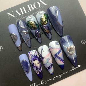 Puede incluir: Conjunto de diez uñas postizas con varios diseños. Las uñas están decoradas con mariposas, purpurina y una pedrería en forma de corazón. El texto "Nailbox you love it we nail it" es visible en la esquina superior izquierda de la imagen. El texto "Thank you for your order" es visible en la esquina inferior derecha de la imagen.