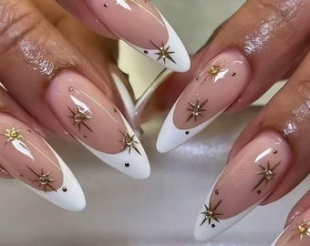 Puede incluir: Uñas en forma de almendra con un diseño de manicura francesa clásica con puntas blancas sobre una base nude. Cada uña está decorada con pequeños detalles de estrellas doradas metálicas y diminutos tachones oscuros circulares.