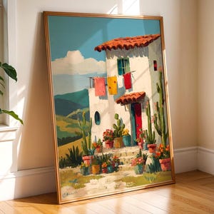 May include: A framed painting depicts a white stucco house with a red-tiled roof and a red door. Colorful potted plants and cacti adorn the front steps. The artwork features a blue sky, green hills, and hanging laundry.