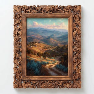 May include: A framed landscape painting depicting a mountainous valley scene with a dirt road winding through the hills. The painting is in a detailed, ornate, brown wooden frame. The artwork features a color palette of blues, greens, and browns.