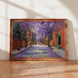 Puede incluir: Pintura enmarcada que representa una calle empedrada bordeada de árboles en plena floración con flores moradas. La obra de arte tiene una paleta de colores cálidos, con edificios en tonos anaranjados y un marco de madera oscura.