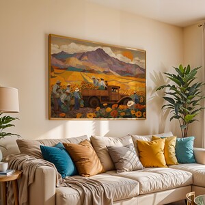 May include: A framed painting depicts a harvest scene with a truck in a sunflower field, mountains, and a setting sun. The painting hangs above a beige sectional sofa with colorful throw pillows. A lamp and potted plant are on a side table.