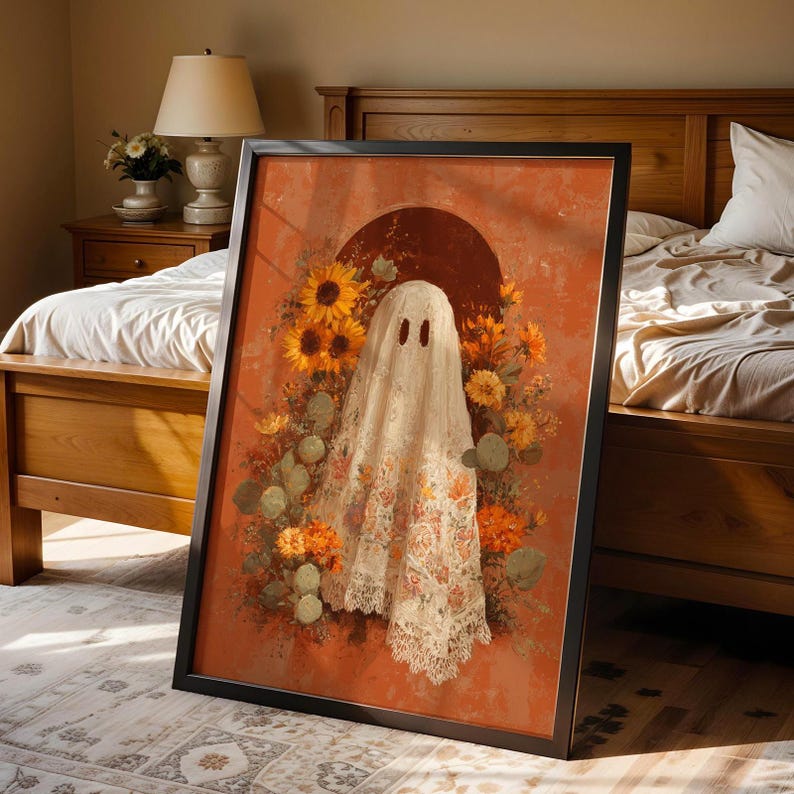 May include: Framed art print featuring a whimsical ghost figure draped in a floral patterned cloth, set against a warm orange backdrop. Sunflowers and other autumnal flowers surround the ghost, creating a unique and artistic Halloween theme.