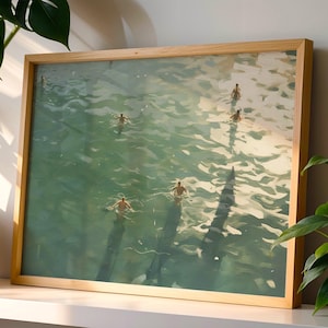 Pode incluir: Impressão artística emoldurada que retrata pessoas nadando em água turquesa. A obra de arte está em uma moldura de madeira marrom clara. A luz do sol reflete na superfície da água, criando sombras e destaques. Cena de verão serena.